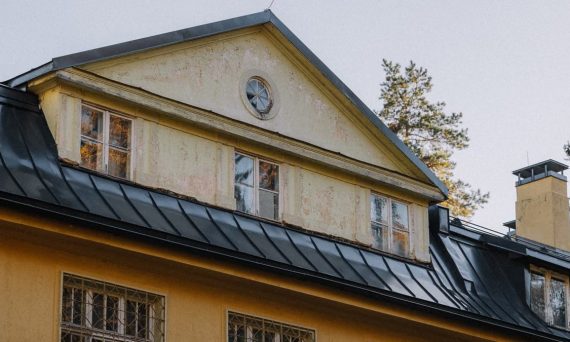 Close-up of a vintage house with a rustic yellow facade and black metal roof in an autumn setting.
